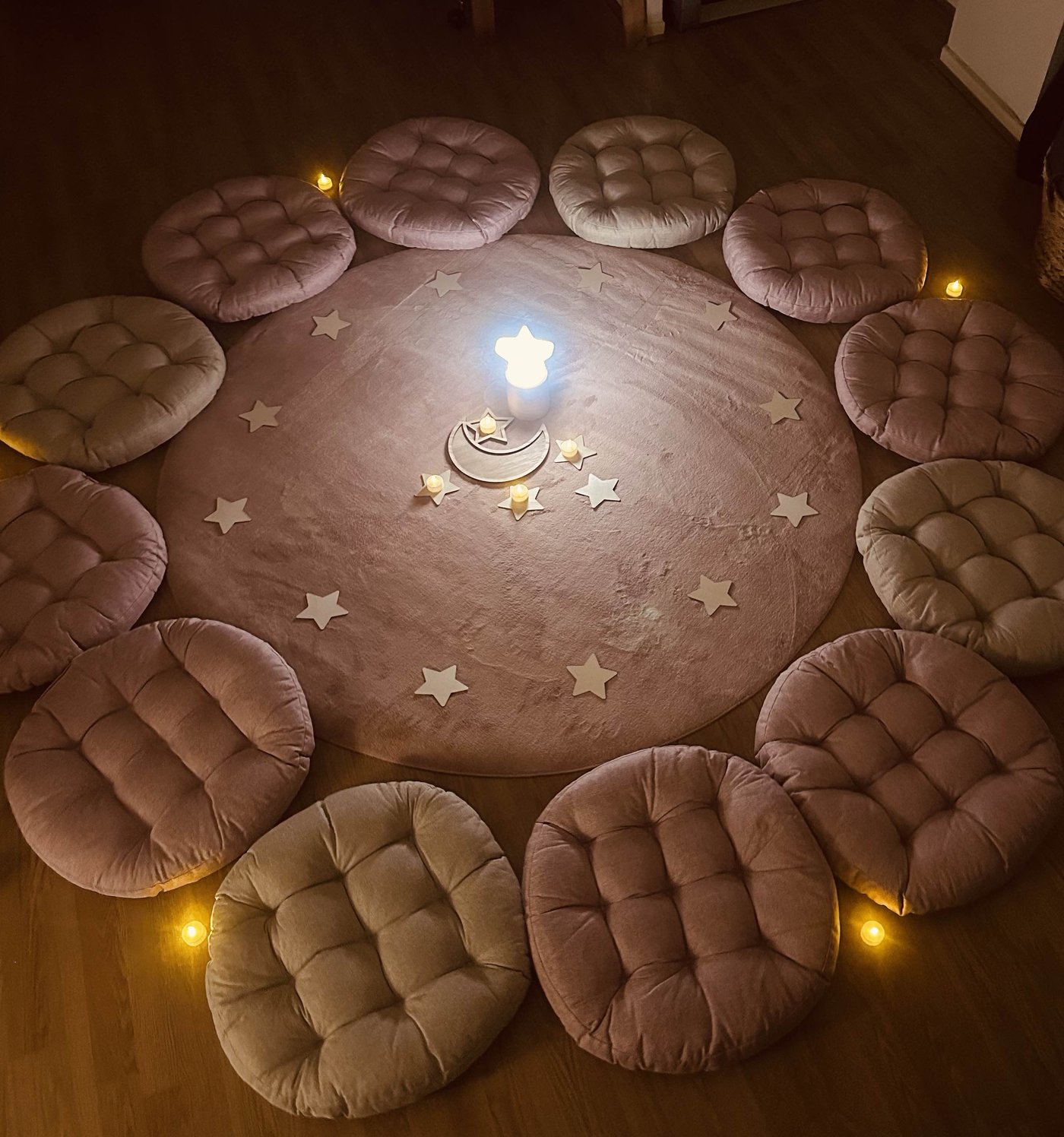 Cercle de coussins autour d'un tapis étoilé avec une veilleuse lune en bois et des bougies, décor préparé pour l'atelier